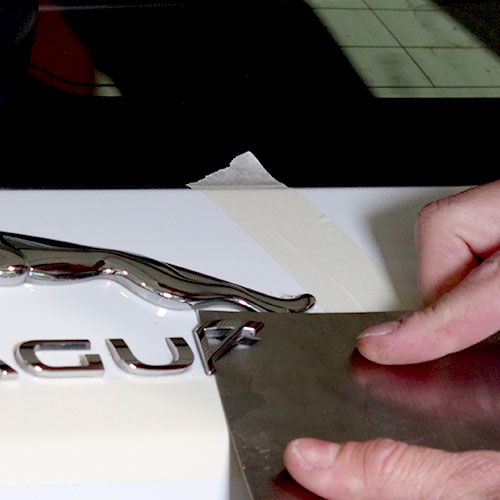 Le logo d'une voiture est enlevé à l'aide d'une spatule